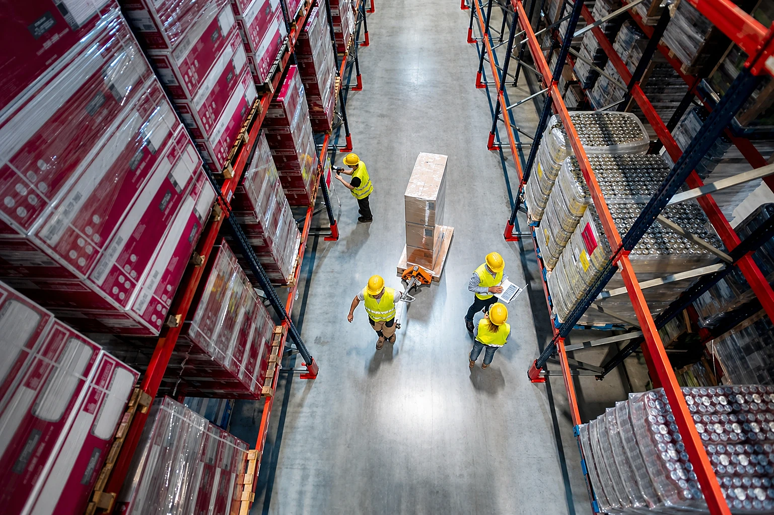 Overhead view of a warehouse aisle with staff in high-visibility vests moving pallets between racking